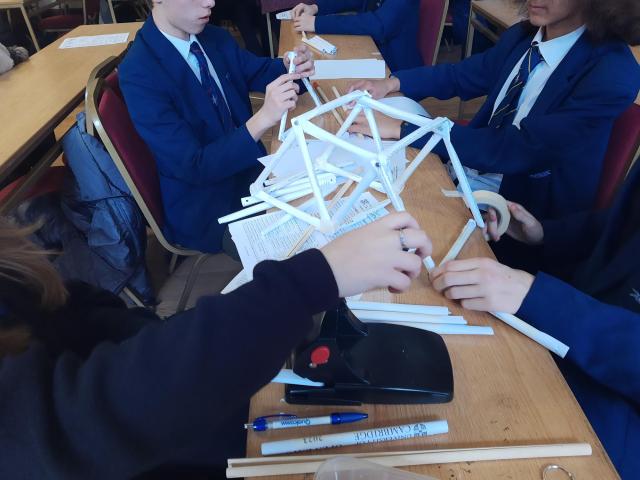 An engineering challenge set for visiting school pupils, showing a group around a table with paper and other stationery 
