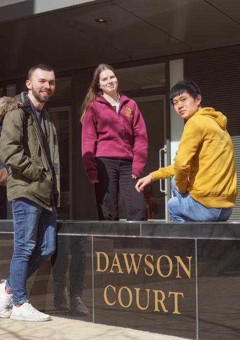 Three students with a sign reading Dawson Court at St Catharine's College